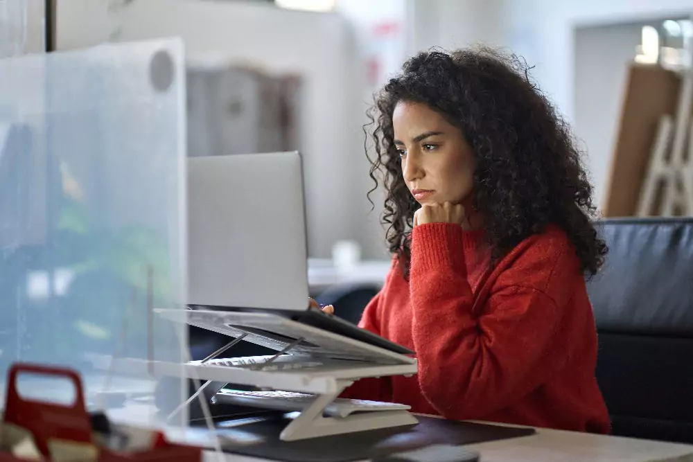 Young latin professional business woman office worker analyst sitting at desk working on laptop watching elearning.